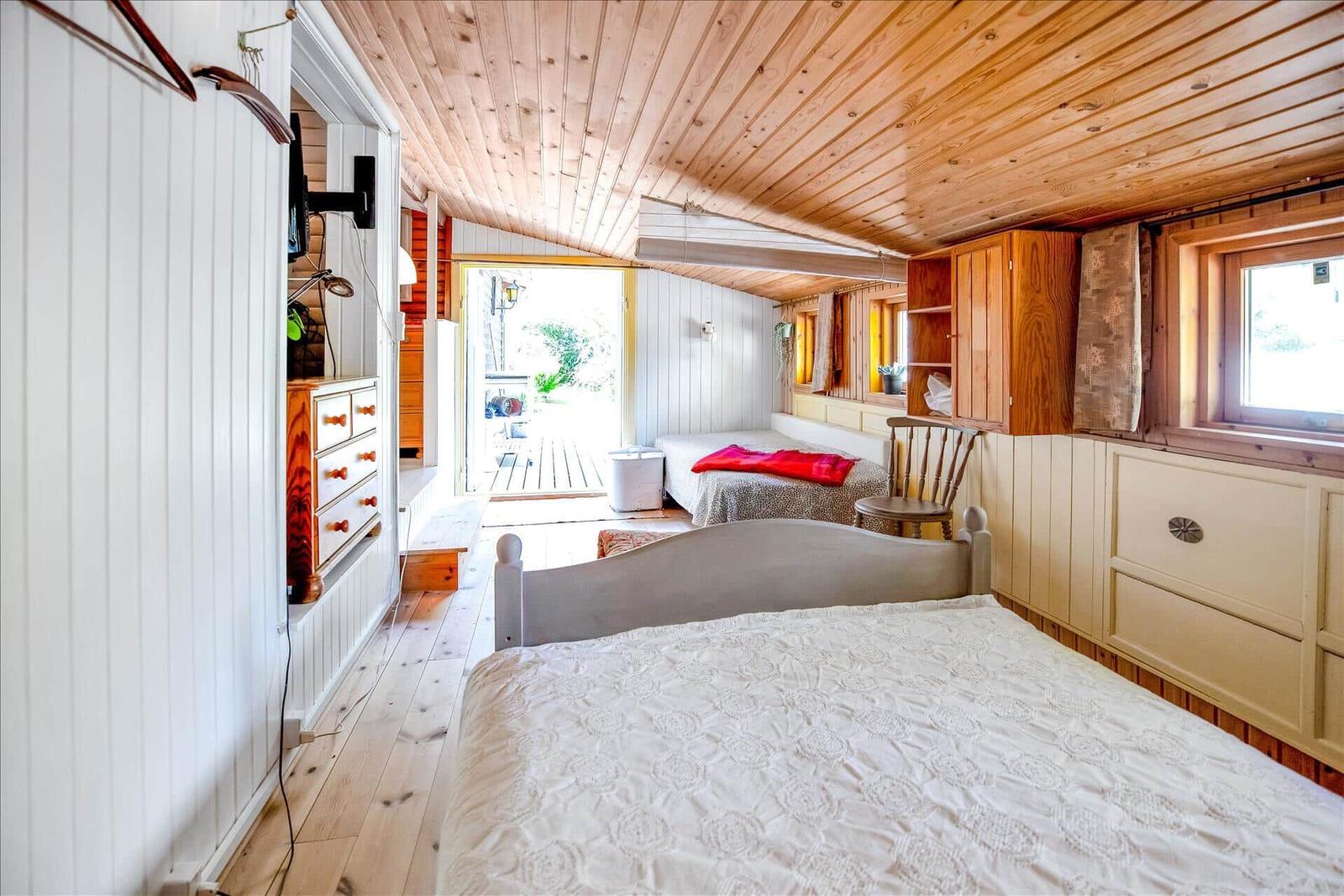 Wohnraum mit rosa Sofa, Holztisch und Sessel. Weiße Holzwände und Decke.