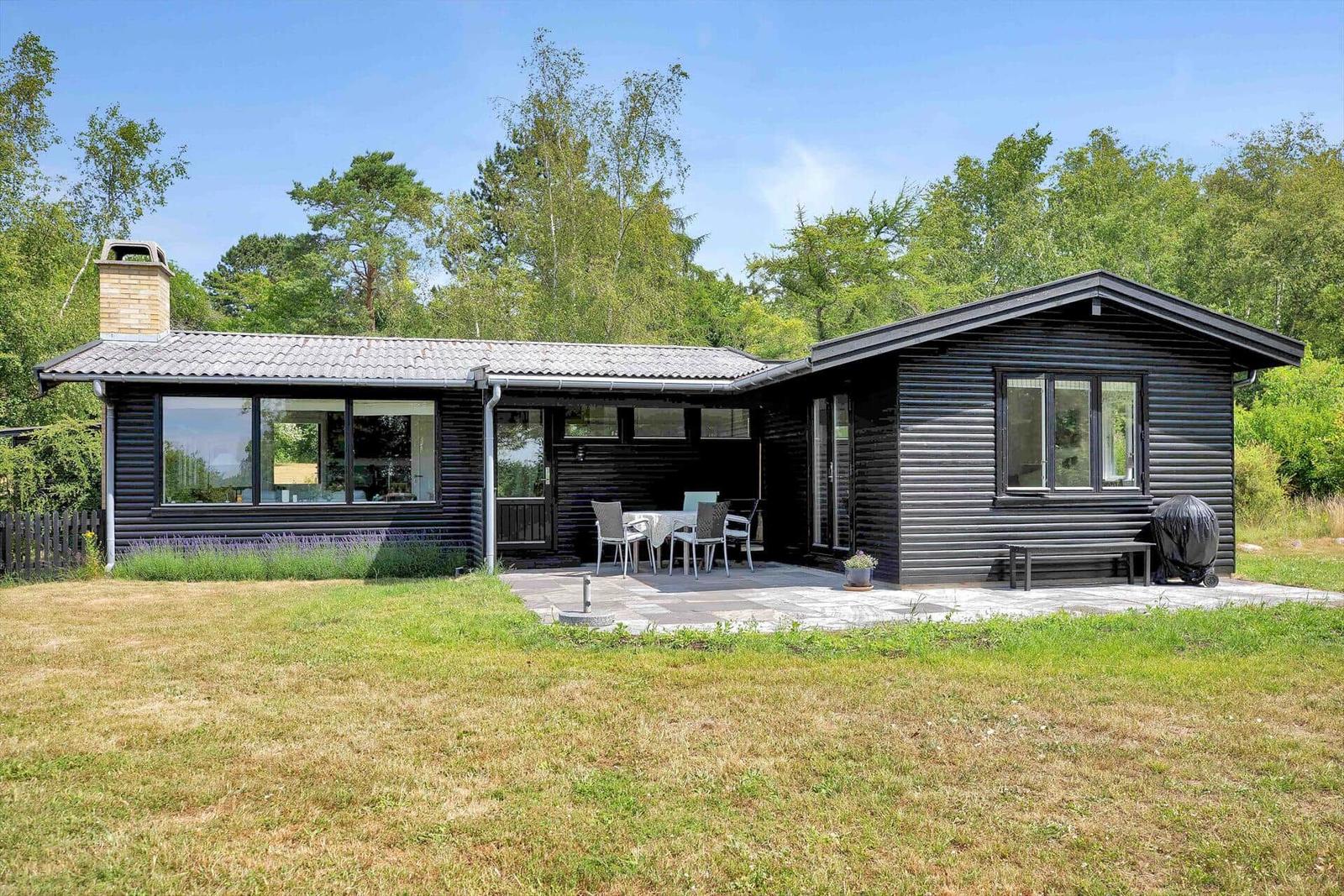Terrasse mit Tisch und Stühlen, Gartenhaus und grüner Umgebung.