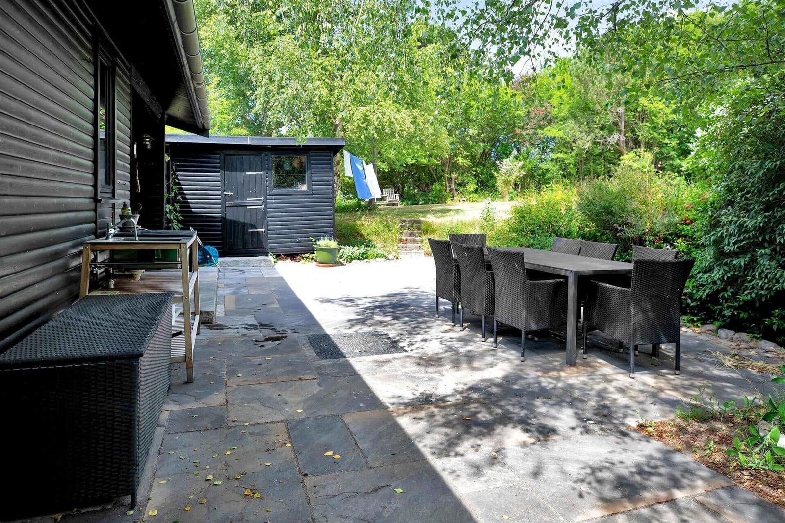 Ein Weg aus Steinplatten führt durch einen grünen Garten zu einem Holzhaus mit Fenster.