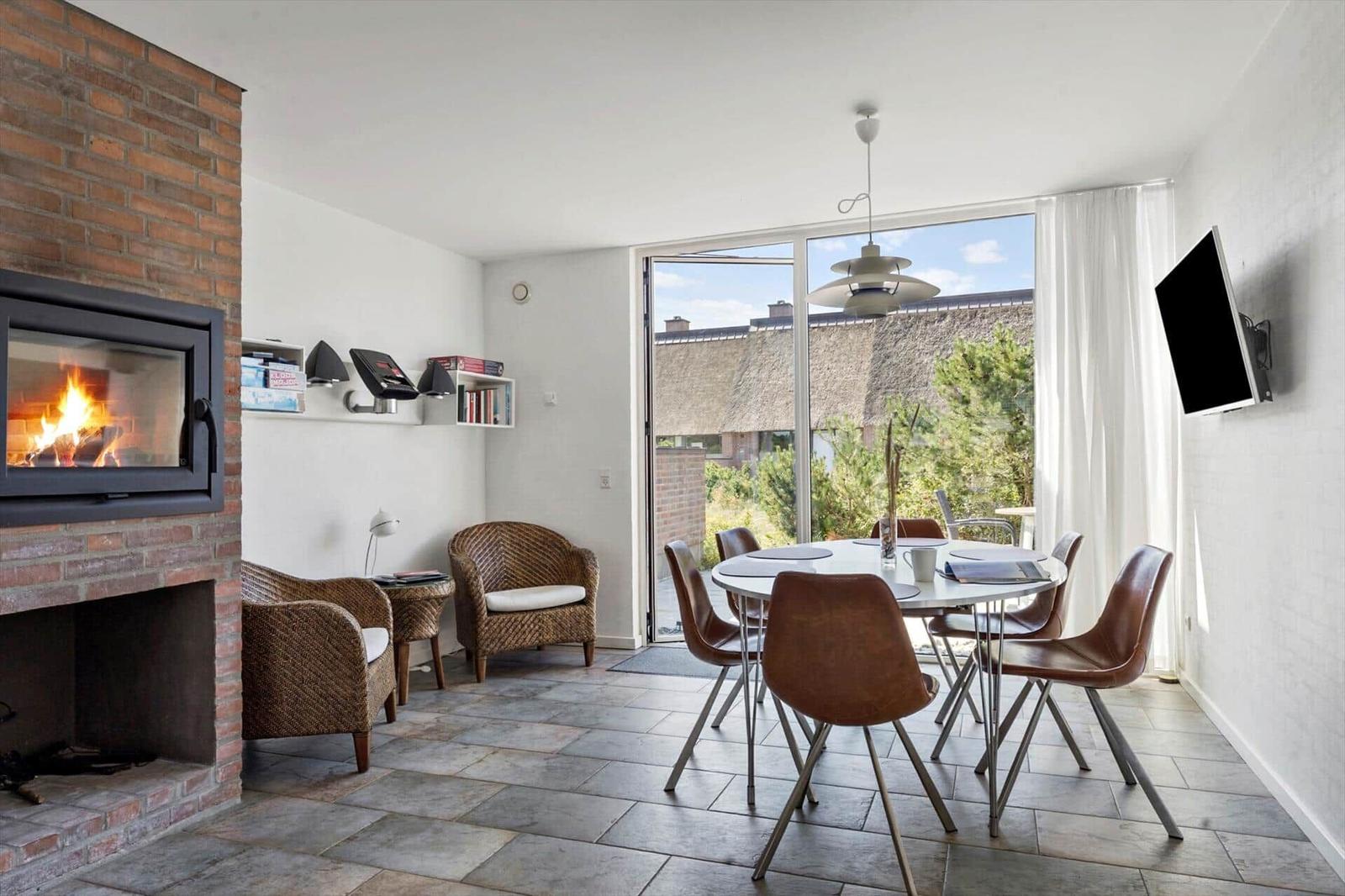 Wohnzimmer mit Sitzgelegenheiten, Fernseher und Blick auf Balkon mit Gartenmöbeln.