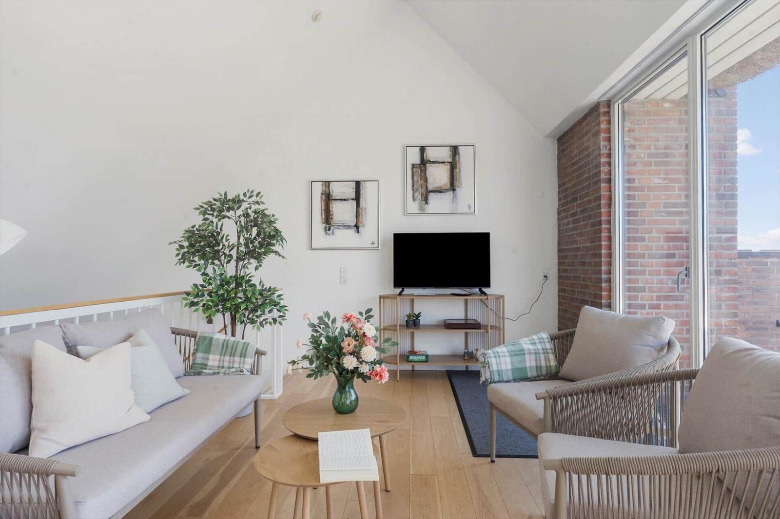 Wohnzimmer mit Sofa, Sessel, Tisch, Blumen und Fernseher.