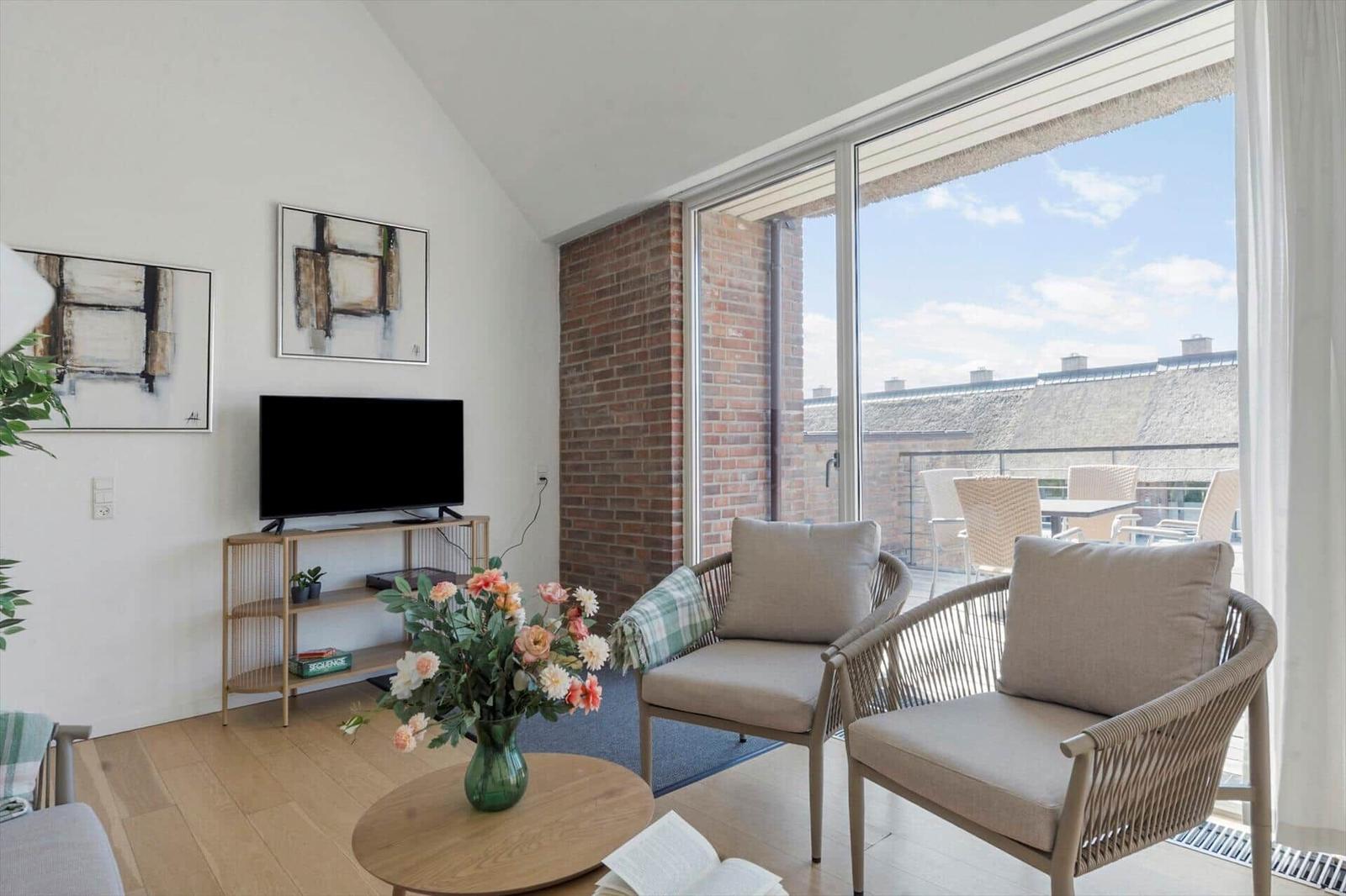 Wohnzimmer mit Sofa, Sessel, TV und Pflanzen. Holzboden und weiße Wände.