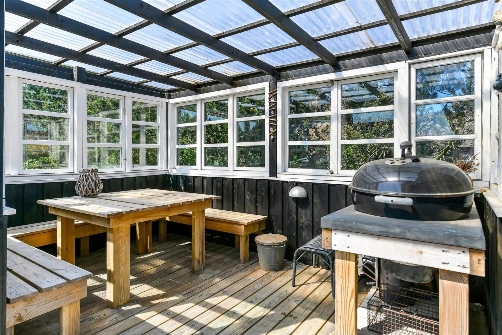 Terrasse mit Grill, Tisch und Stühlen unter einem Dach.