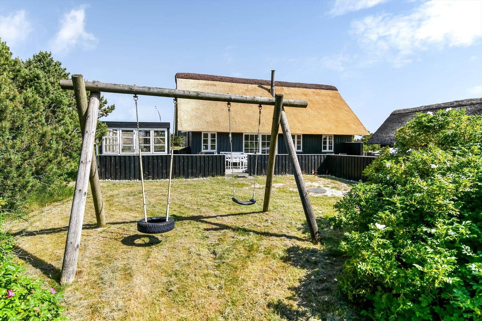Holzschaukel mit Reifen und Sitz im Gras vor Bäumen.