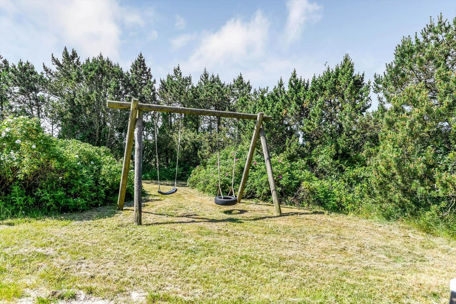 Holzhäuschen mit Strohdach und Holzterrasse in grüner Umgebung.