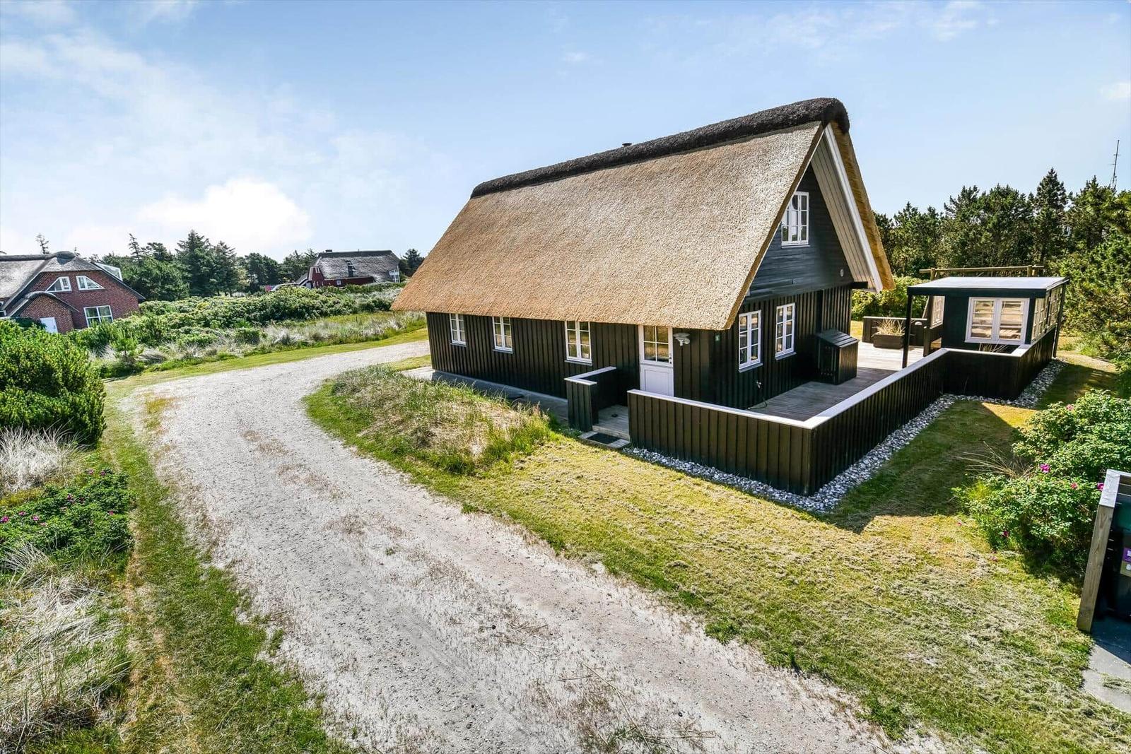Haus mit Strohdach, weißer Tür und Holzveranda im Grünen.