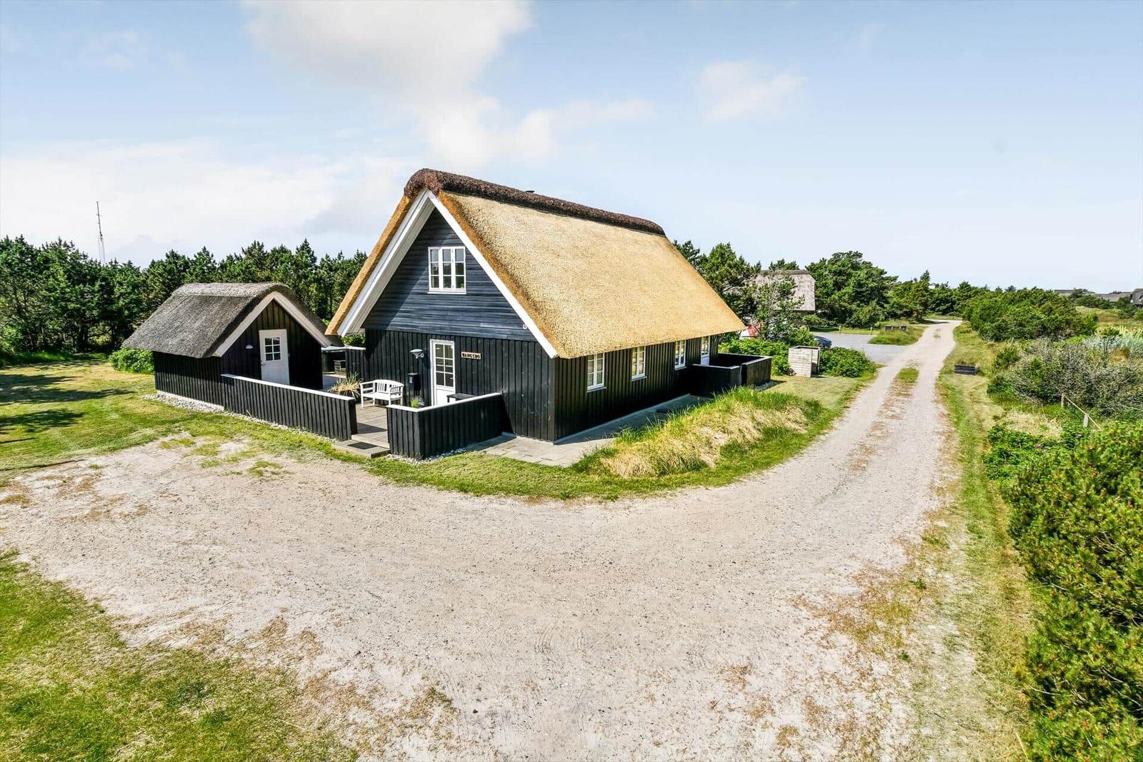 Haus mit strohgedecktem Dach und weißem Gartenmöbelset auf Terrasse.