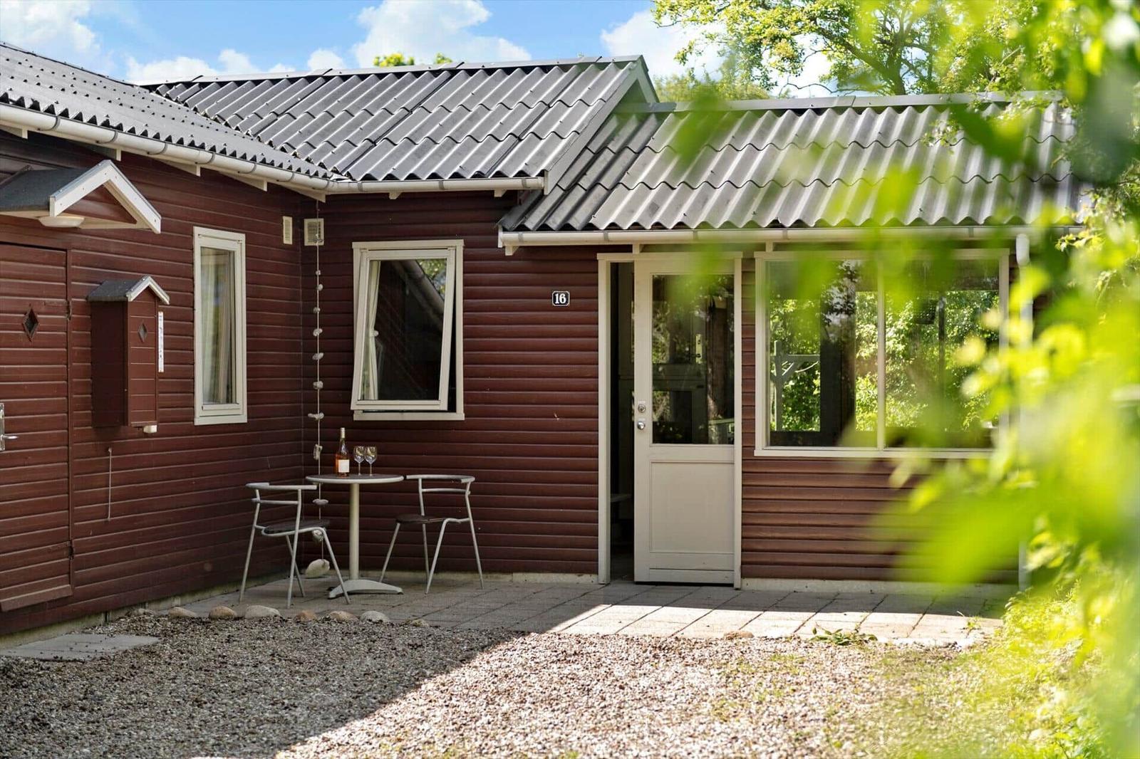 Roter Holzaufbau mit Terrasse, Sonnenschirm und Tisch. Gartentür führt ins Haus.
