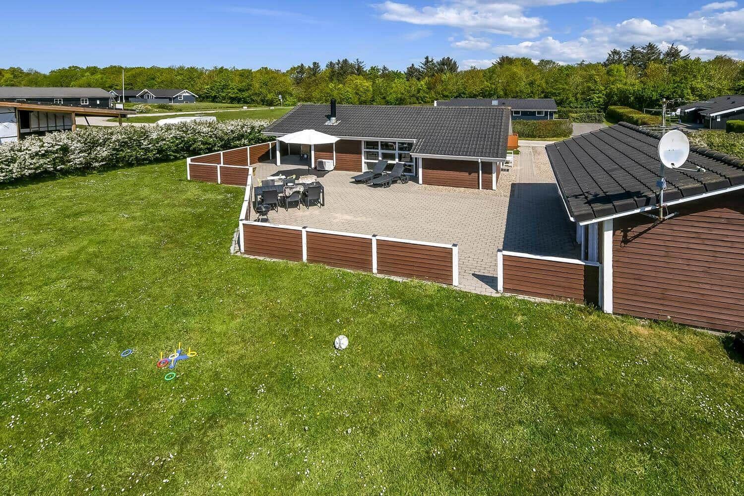 Haus mit Terrasse, Garten und Spielzeug auf Rasen.