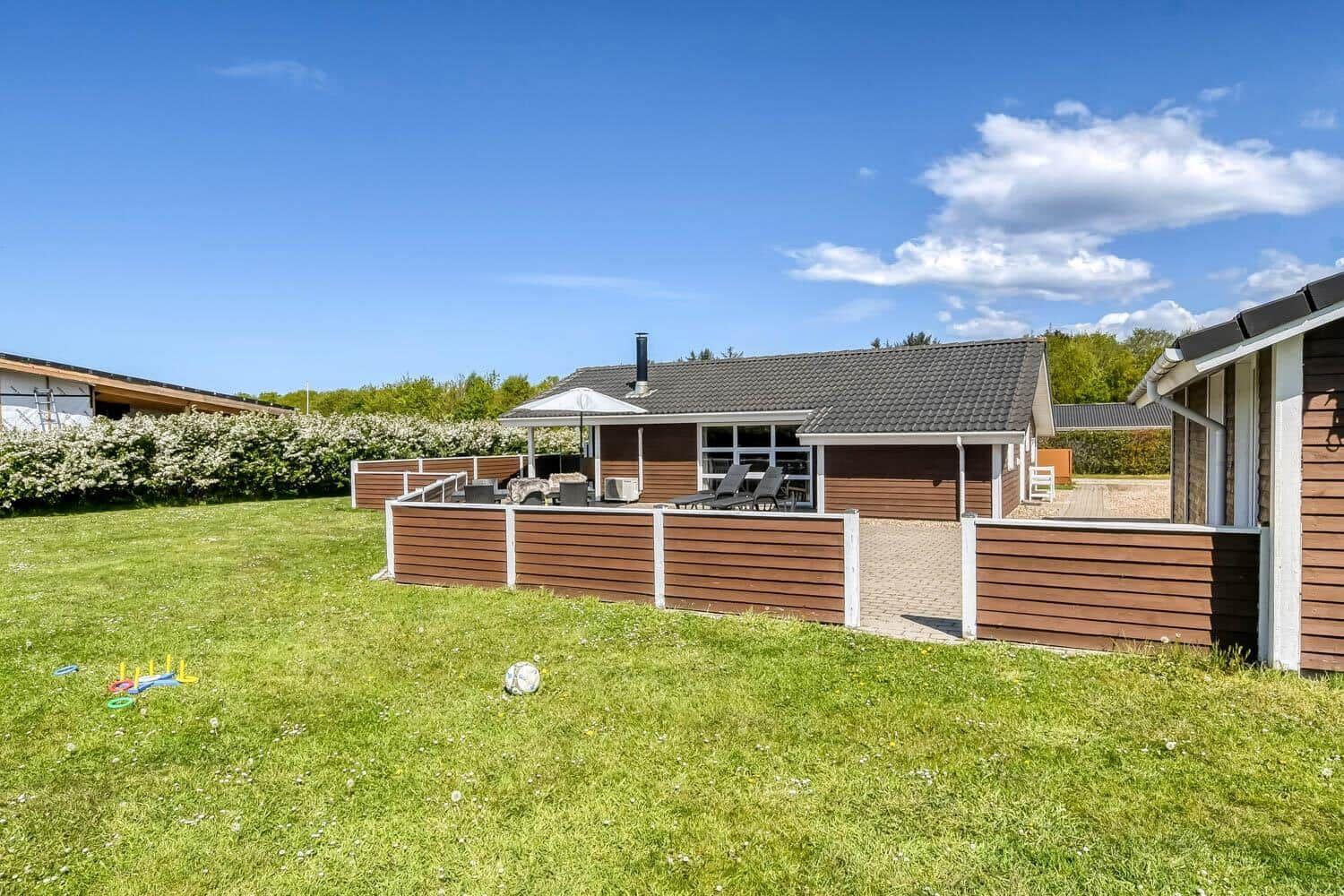 Terrasse mit Grill, Tisch, Stühlen und Liegen vor einem Holzhaus mit Dach.