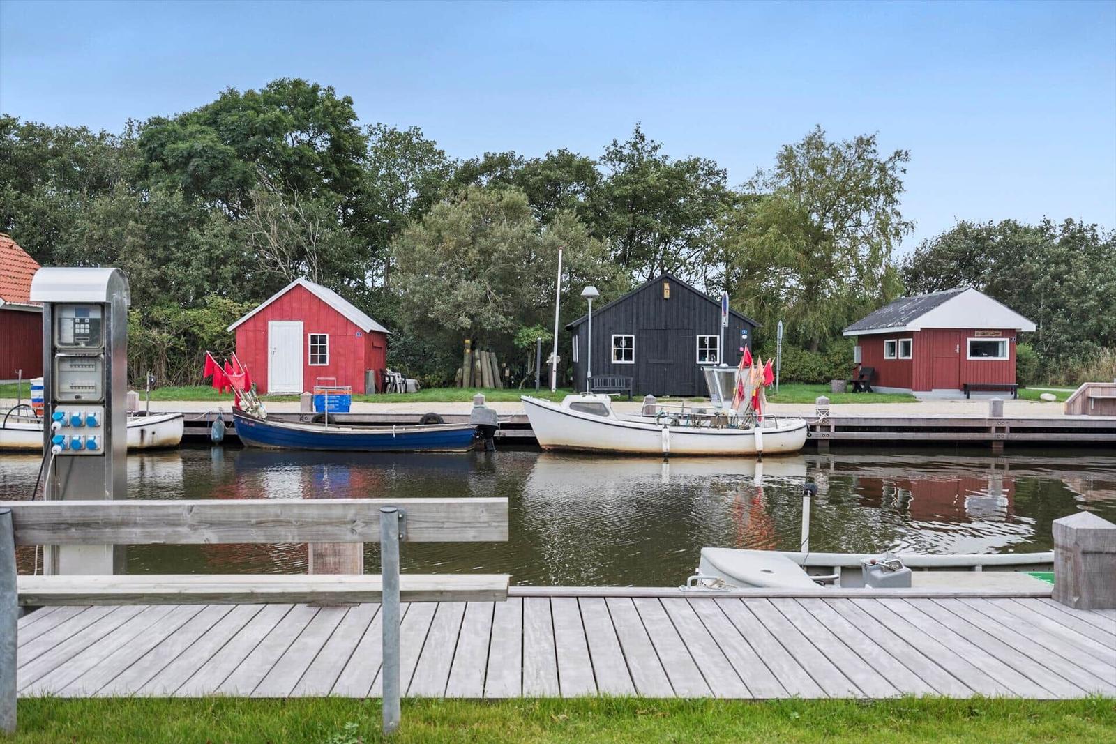 Holzsteg führt zu einem Hafen mit Booten und einer blauen Krananlage.