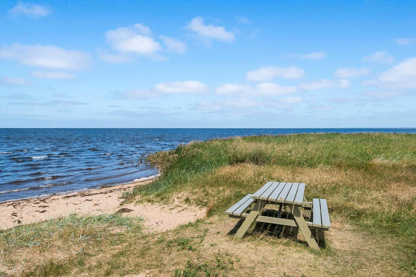 Zwei Holztische stehen am Strand neben einem Steg ins Wasser.