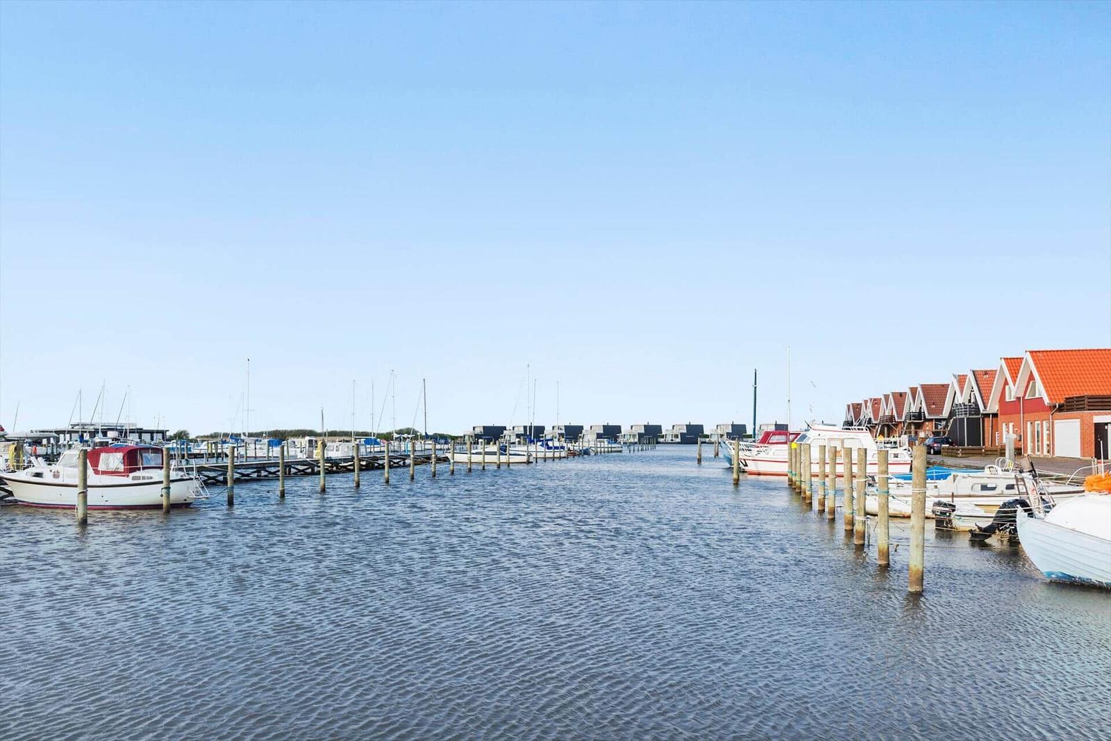 Strand mit Picknicktischen, Grasfläche und Wasser unter blauem Himmel mit Wolken.