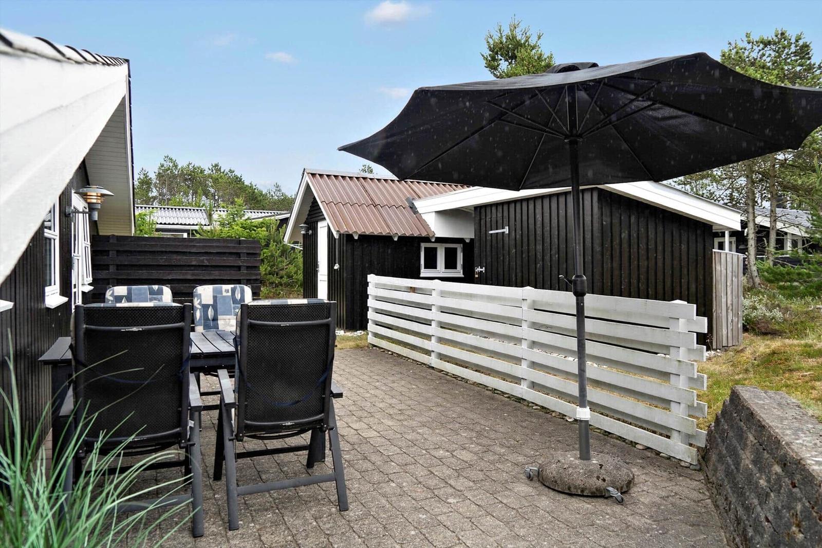 Ein schwarz verkleidetes Ferienhaus mit Dach und Fenstern. Im Vorgarten steht ein Tisch mit Stühlen.