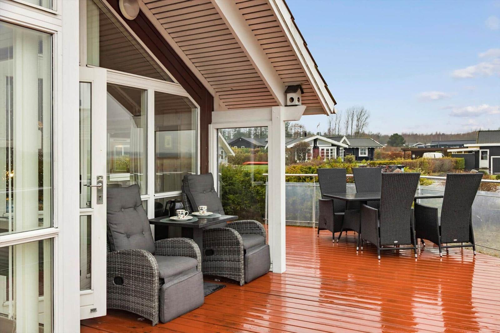 Ein rotes Haus mit Terrasse und Garten. Umgeben von Grünflächen und weiteren Häusern.