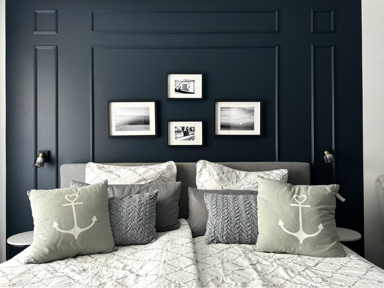 Schlafzimmer mit dunkelblauer Wand, Bett mit Kissen und Wandbildern.