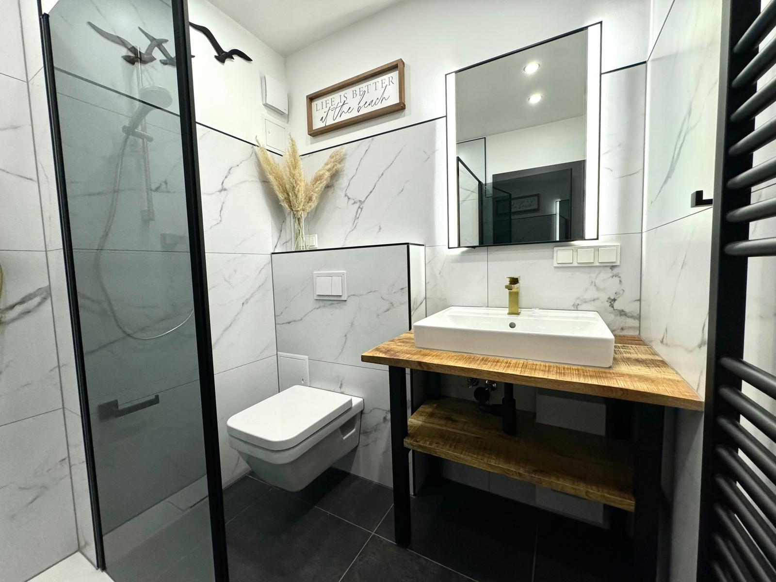 Badezimmer mit Dusche, Waschbecken und Toilette. Weiße Marmorwand und Holzunterschrank.