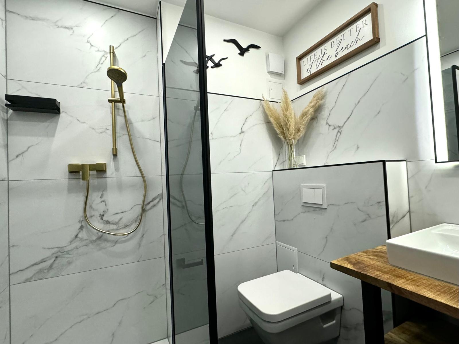 Bad mit Dusche, Toilette und Waschbecken auf Holzunterlage.