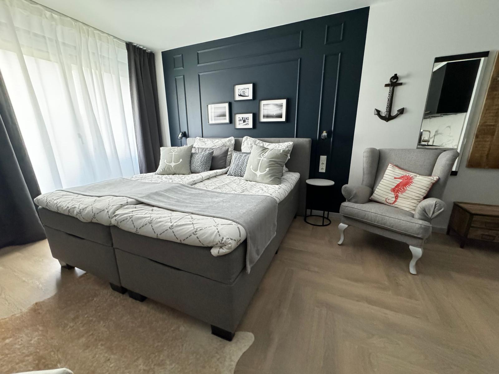 Schlafzimmer mit Bett, Sessel und Ankerdekoration an der Wand.