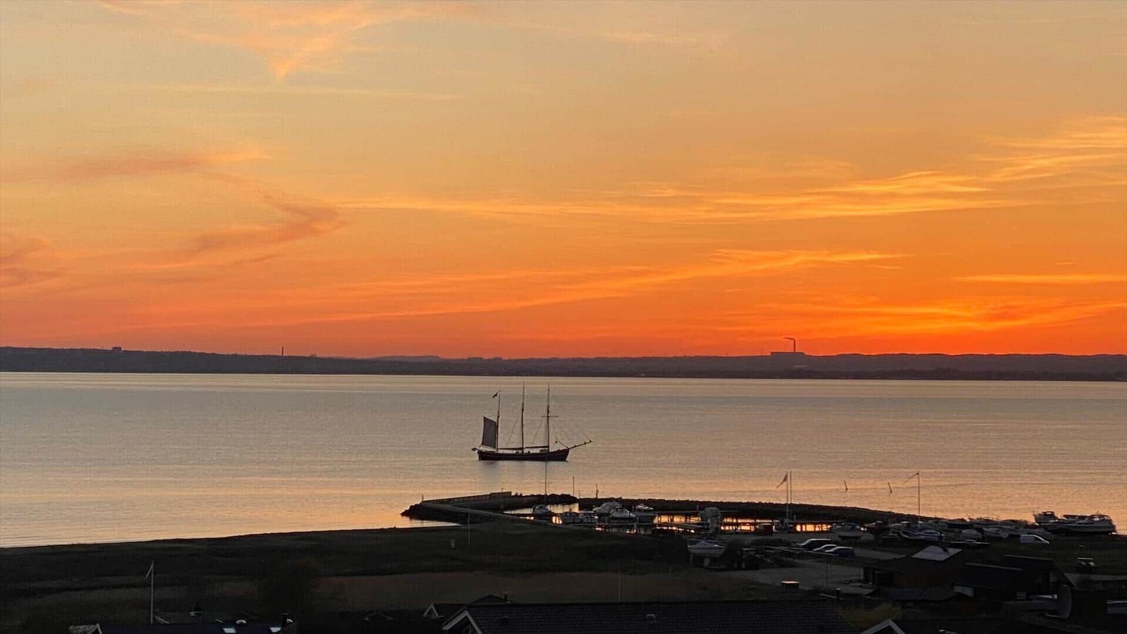 Durch einen Holzbogen blickt man auf einen grünen Garten und einen See bei Sonnenuntergang.