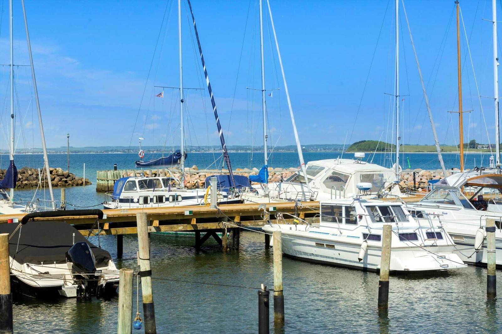 Steiniger Strand mit Wellen, Gras und einem Boot im Hintergrund.