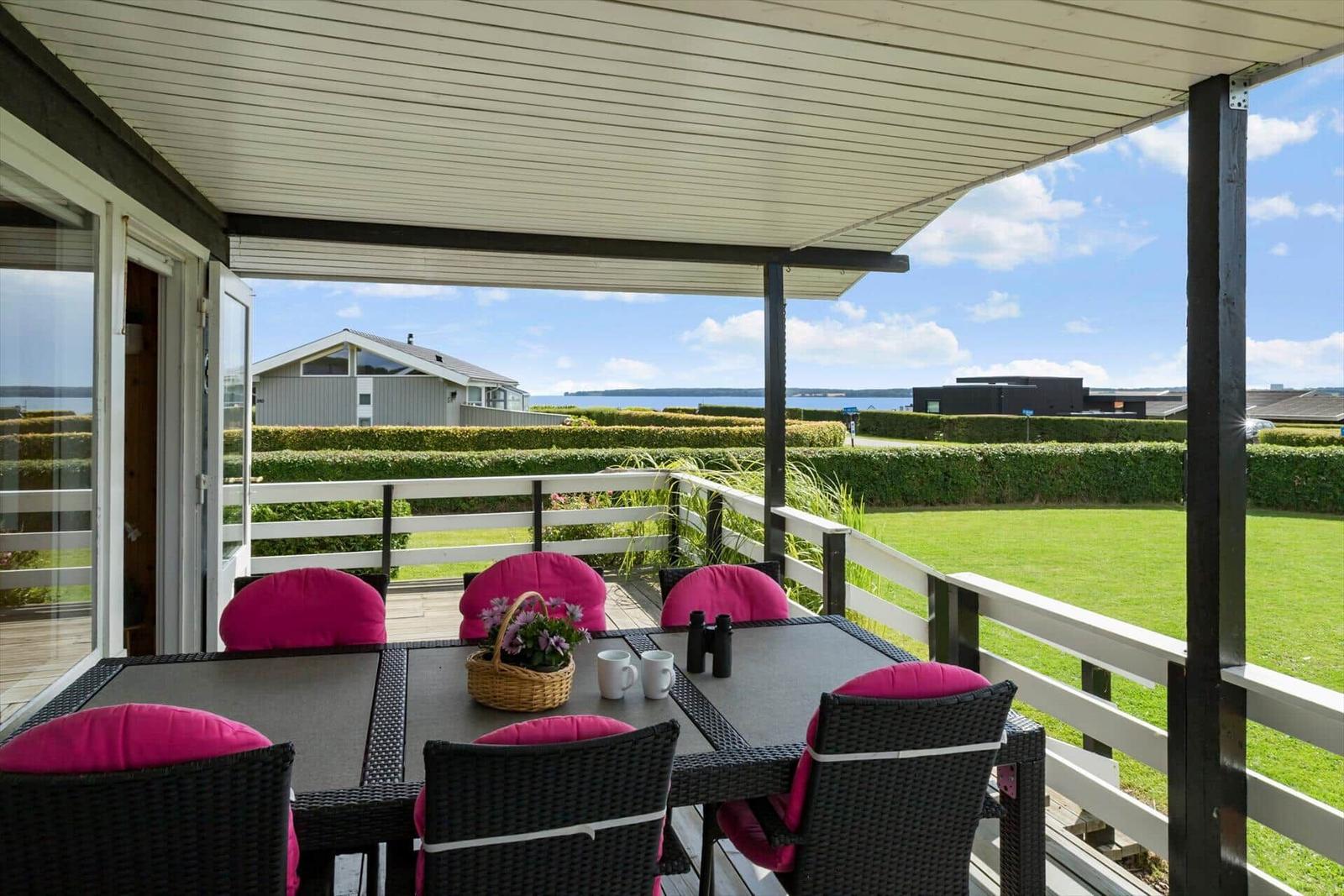 Holzterrasse mit Dusche und Sitzgruppe vor einem dunkel gestrichenen Haus.