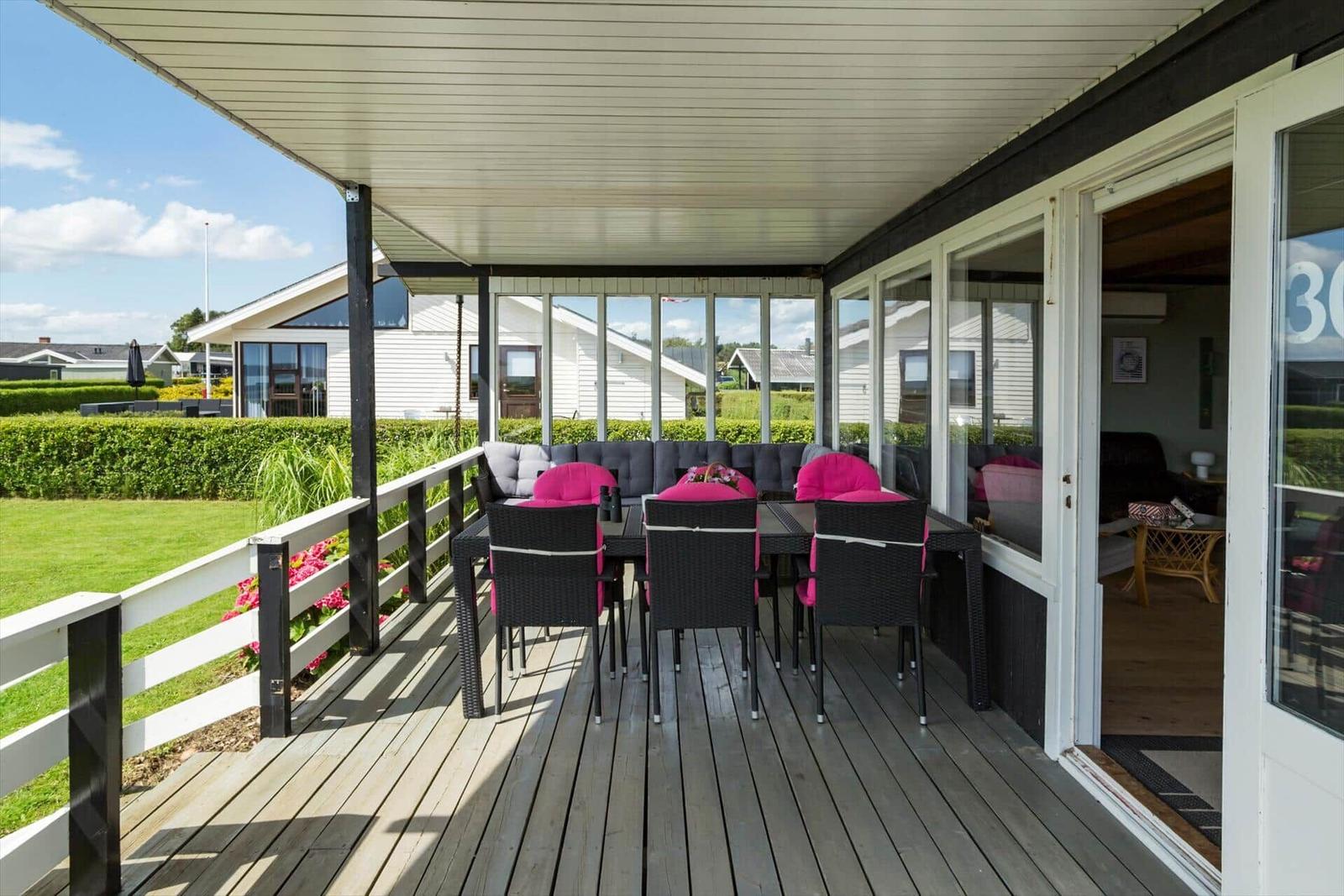 Terrasse mit zwei blauen Sitzmöbeln, Grill und Tisch. Schwarzes Holzhaus mit großem Fenster.