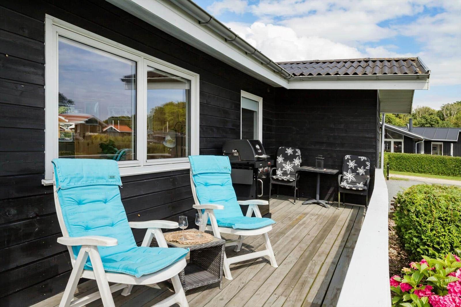 Haus mit Terrasse und Garten. Rote Blumen und grüne Pflanzen umgeben das Gebäude.