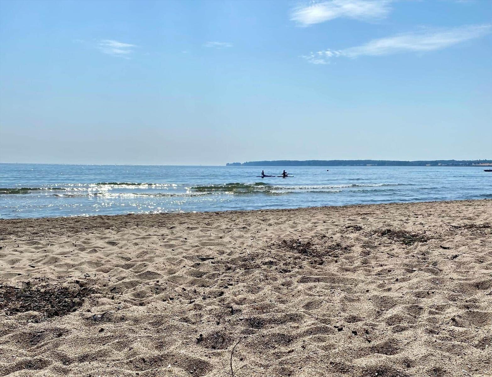 Ein Tor führt zu einem Grünstreifen mit Blick auf das offene Meer unter blauem Himmel.