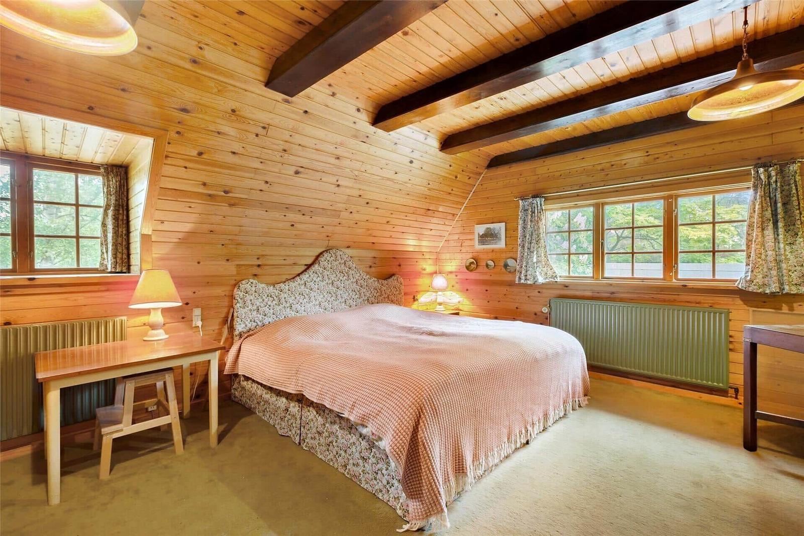 Schlafzimmer mit Holzwand, Fenster, Bett und Schrank