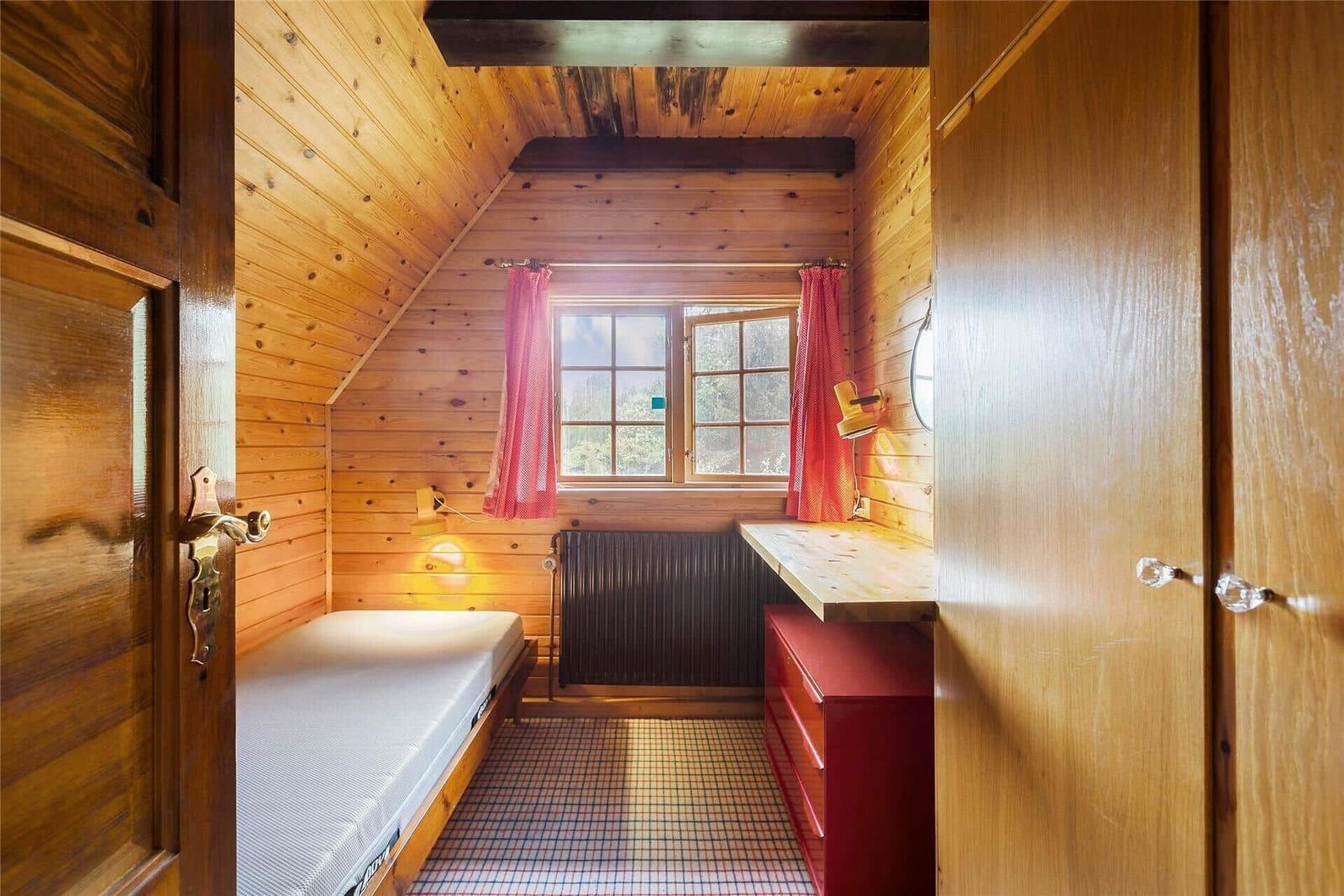 Schlafzimmer mit Holzwand, Bett, Fenster und Heizung.