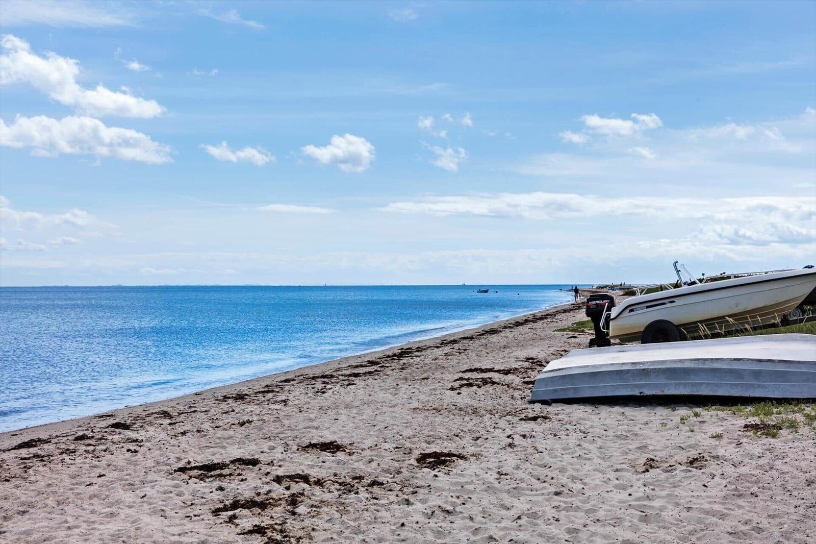 Meerfront mit Strand, Grünflächen und modernen Häusern in der Ferne.