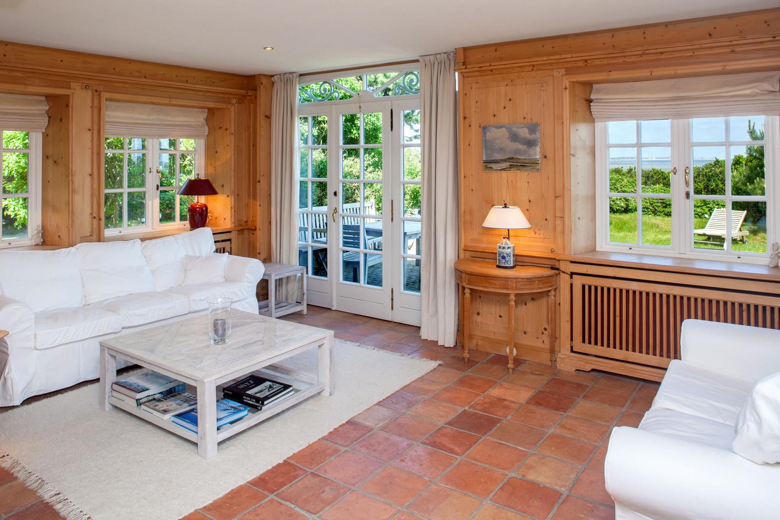 Wohnzimmer mit weißen Sofas, Holzvertäfelung, Terrakottaboden und Gartentür.