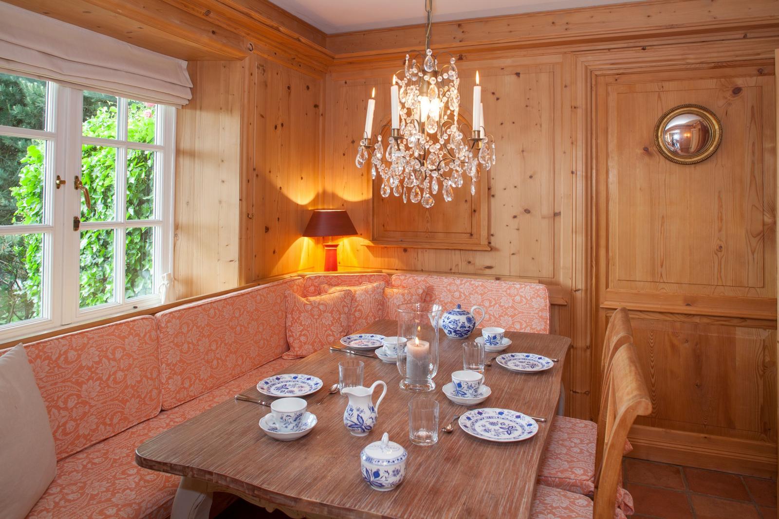 Esszimmer mit Holzvertäfelung, Eckbank, gedecktem Tisch und Kronleuchter.