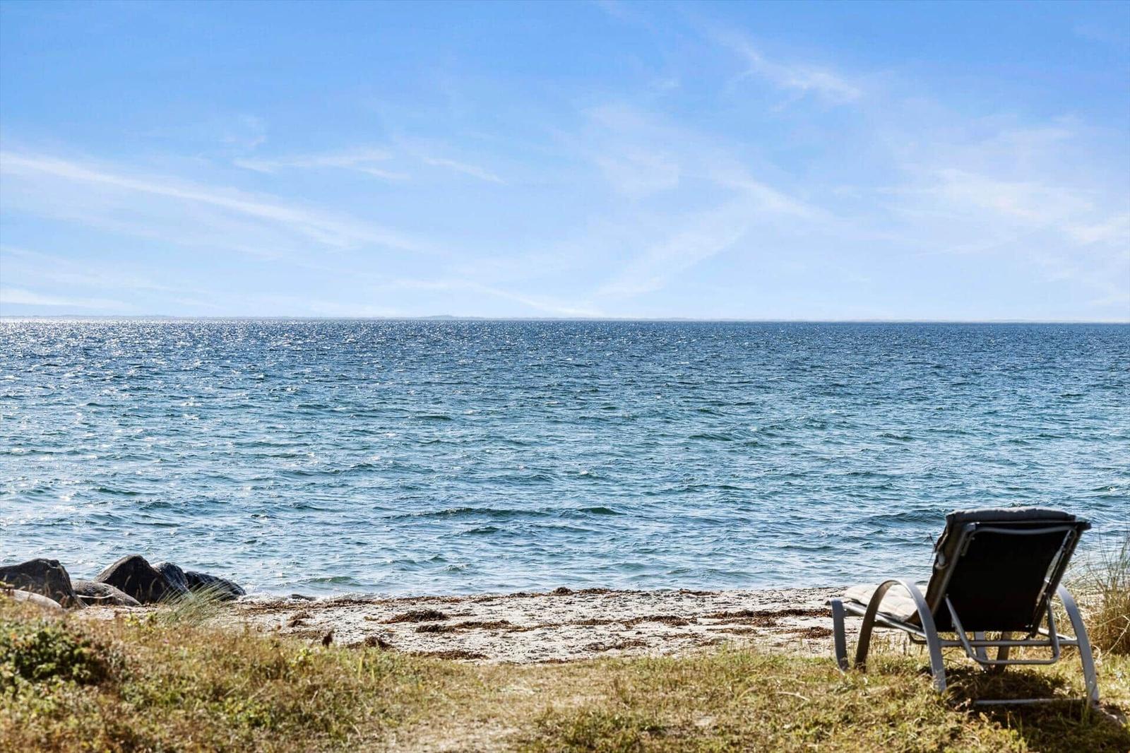Sun lounger in dune grass facing a sandy beach, rocks and open water.