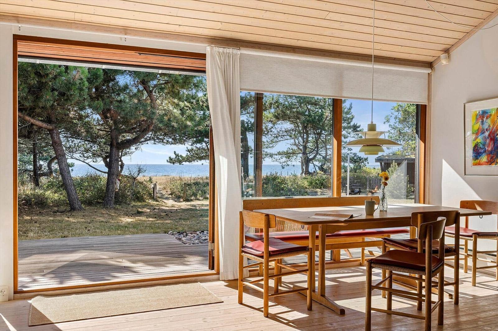Dining room with wooden table, open sliding glass door and a view of water.
