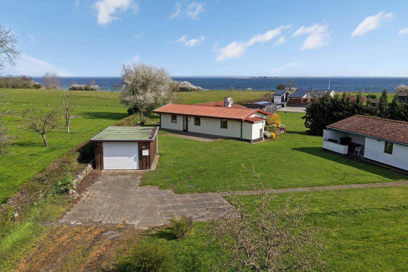 Aerial view of a white house with red roof, lawn, garage and sea.