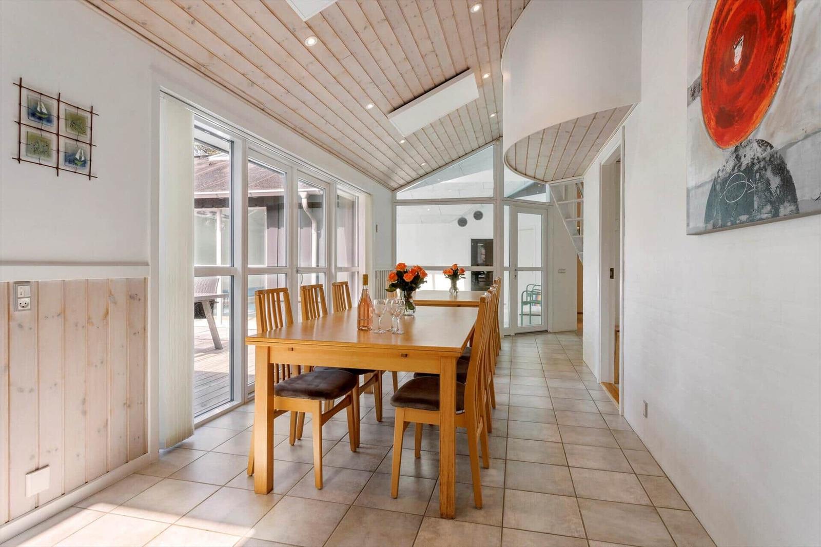 Essbereich mit Holztisch, sechs Stühlen, Rosen und Fensterfront zur Terrasse.