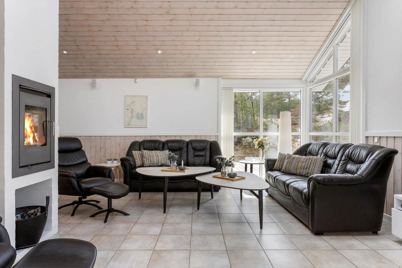 Wohnzimmer mit Kaminofen, schwarzen Ledermöbeln, Couchtischen und Fensterfront.