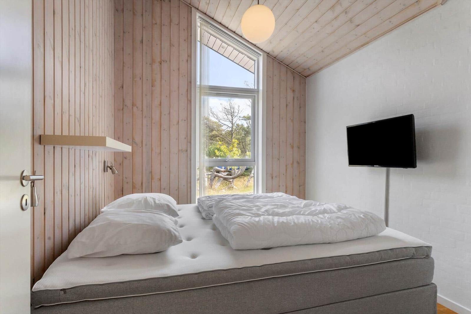 Schlafzimmer mit Doppelbett, Holzvertäfelung, Wand-TV und weißer Kugelleuchte.