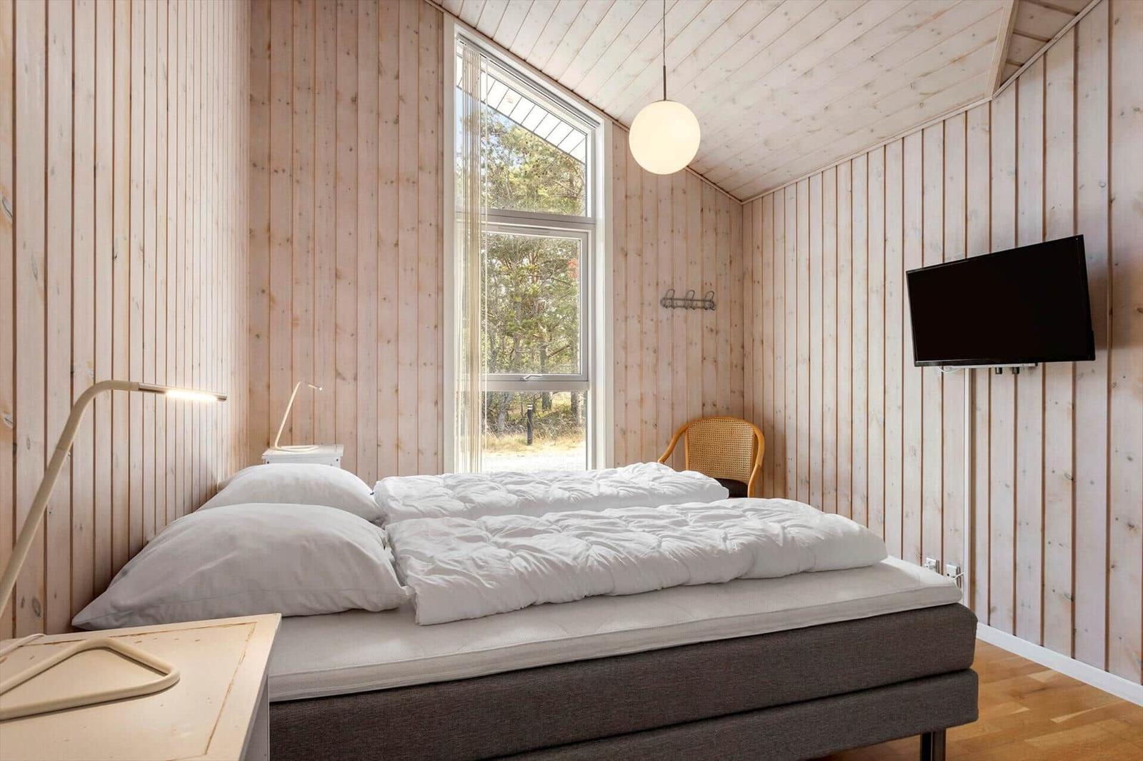 Schlafzimmer mit Holzwänden, Doppelbett, Holzstuhl, Wand-TV und Kugelleuchte.