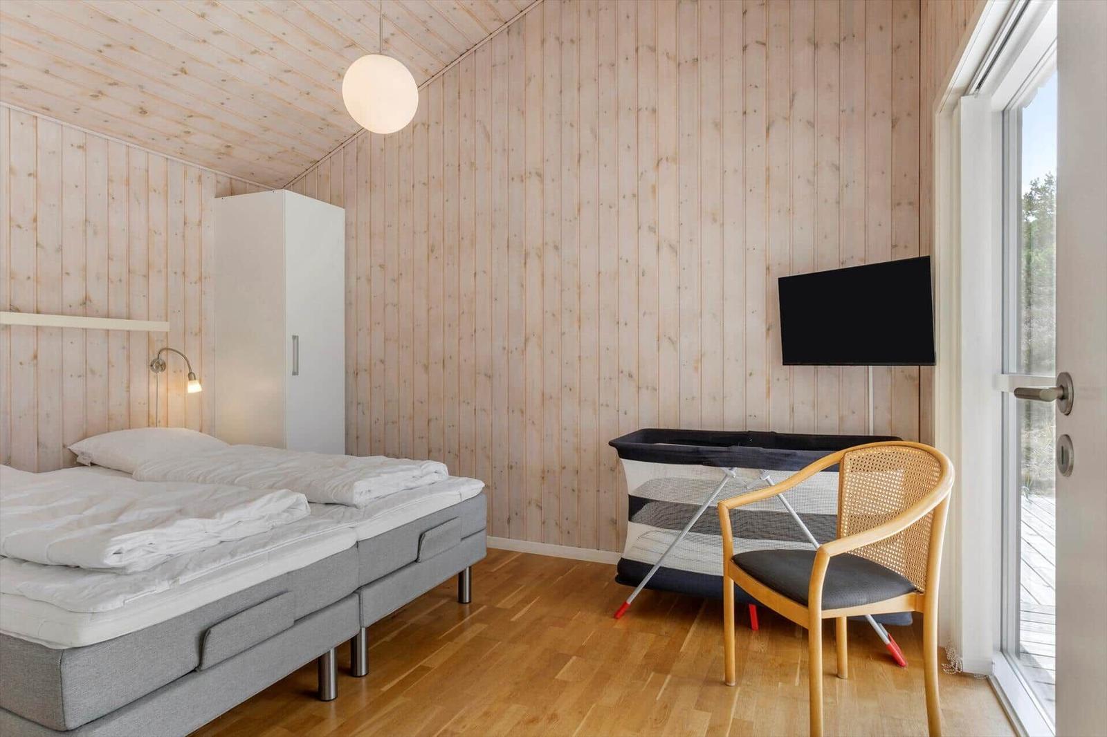 Schlafzimmer mit Bett, Reisebett, weißem Schrank, Korbstuhl und Glastür.