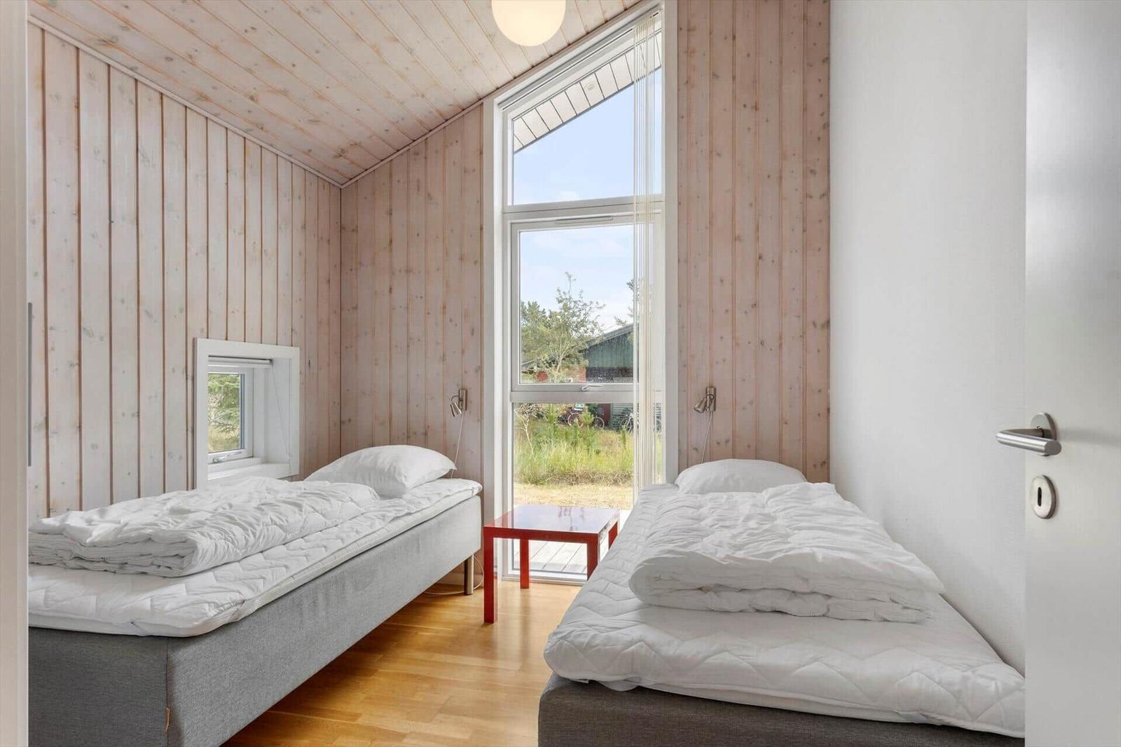 Schlafzimmer mit zwei Einzelbetten, rotem Beistelltisch und bodentiefem Fenster.