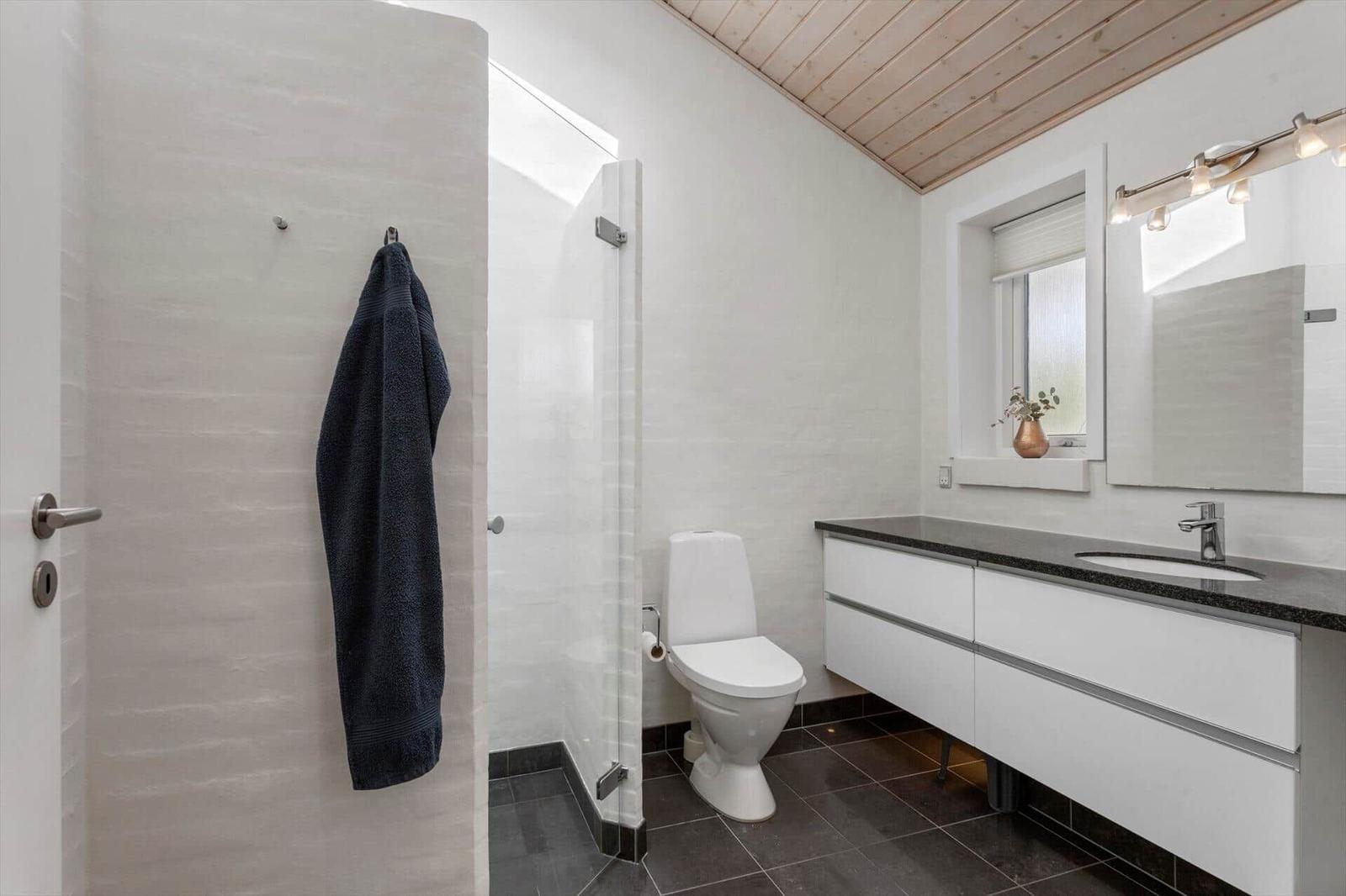 Badezimmer mit weißer Ziegelwand, Waschtisch, WC, Dusche und Holzdecke.