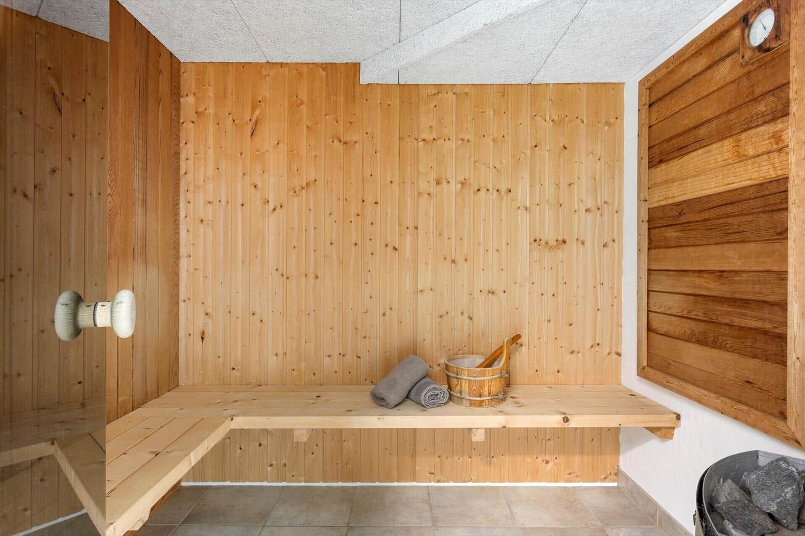 Sauna mit Holzbank, Aufgusskübel, Handtüchern, Ofen und Glastür.