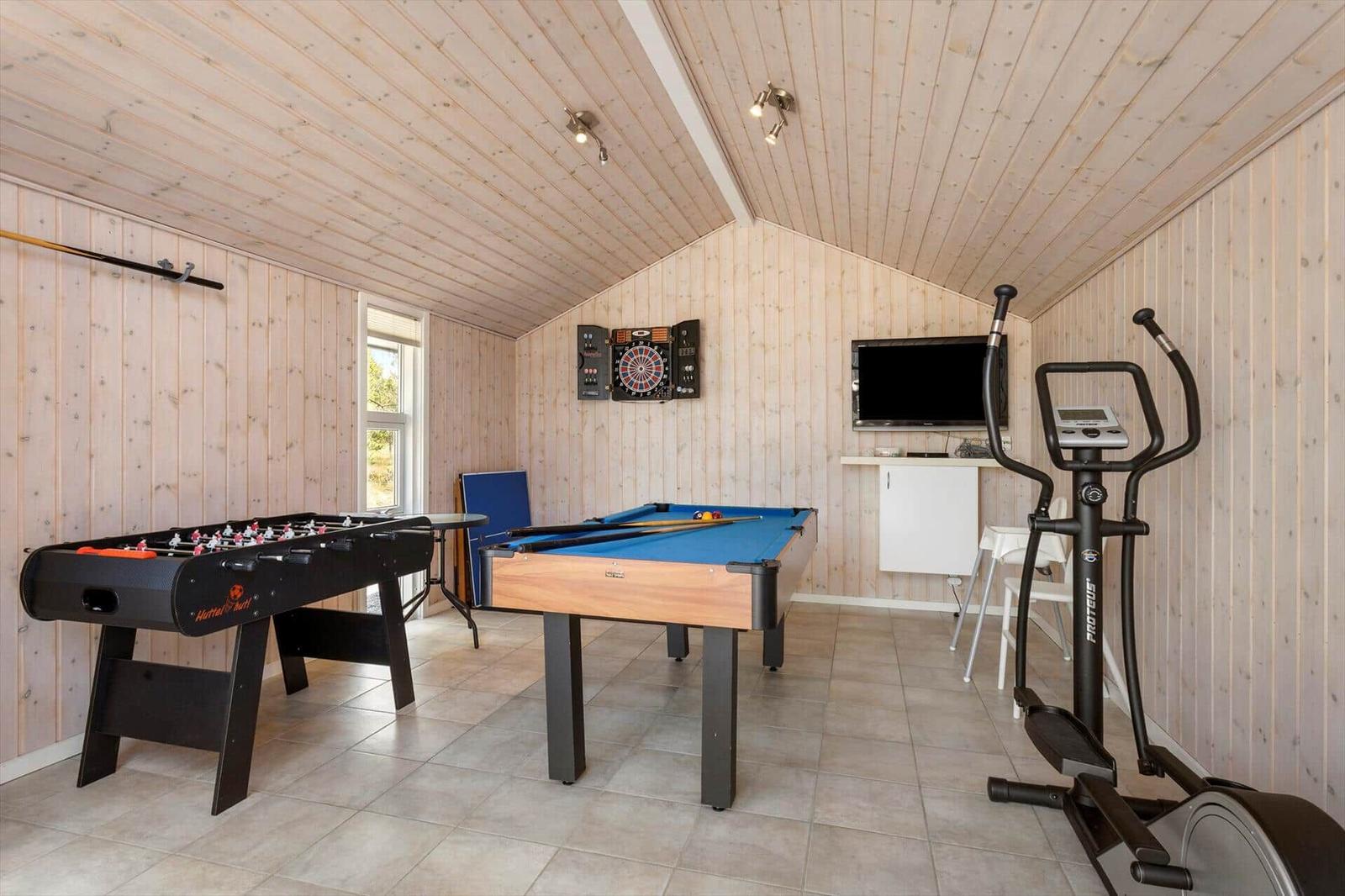 Spielzimmer mit Billardtisch, Kicker, Dartscheibe, Crosstrainer und Fernseher.