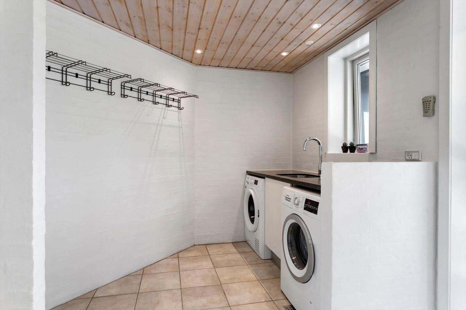 Hauswirtschaftsraum mit Waschmaschine, Trockner, Spüle und Hakenleiste.