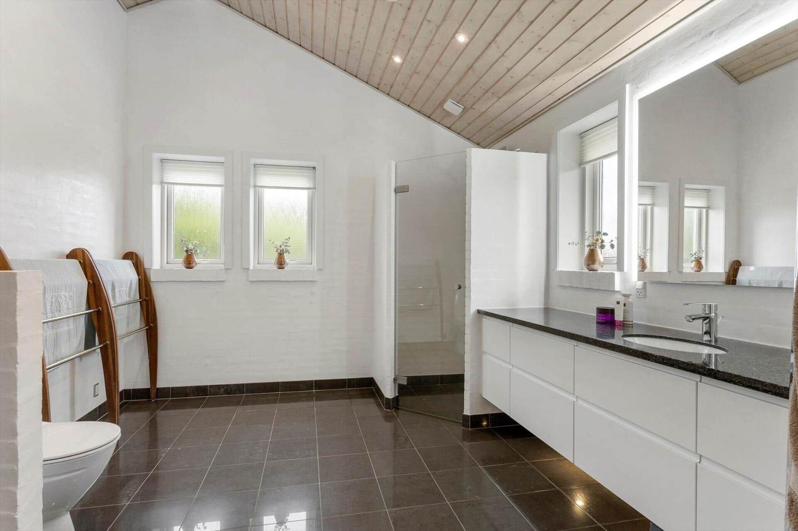 Badezimmer mit Waschtisch, Lichtspiegel, begehbarer Dusche, WC und Holzdecke.