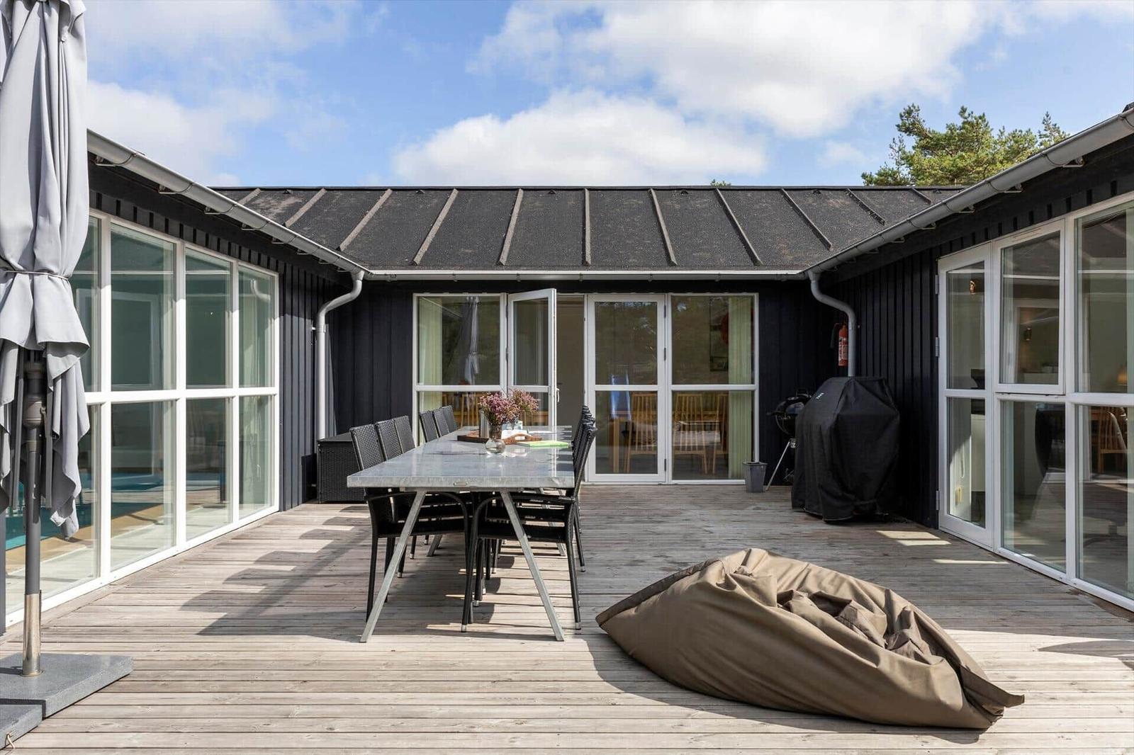 Holzterrasse mit Esstisch, schwarzen Stühlen, Sitzsack und Grill am schwarzen Holzhaus.