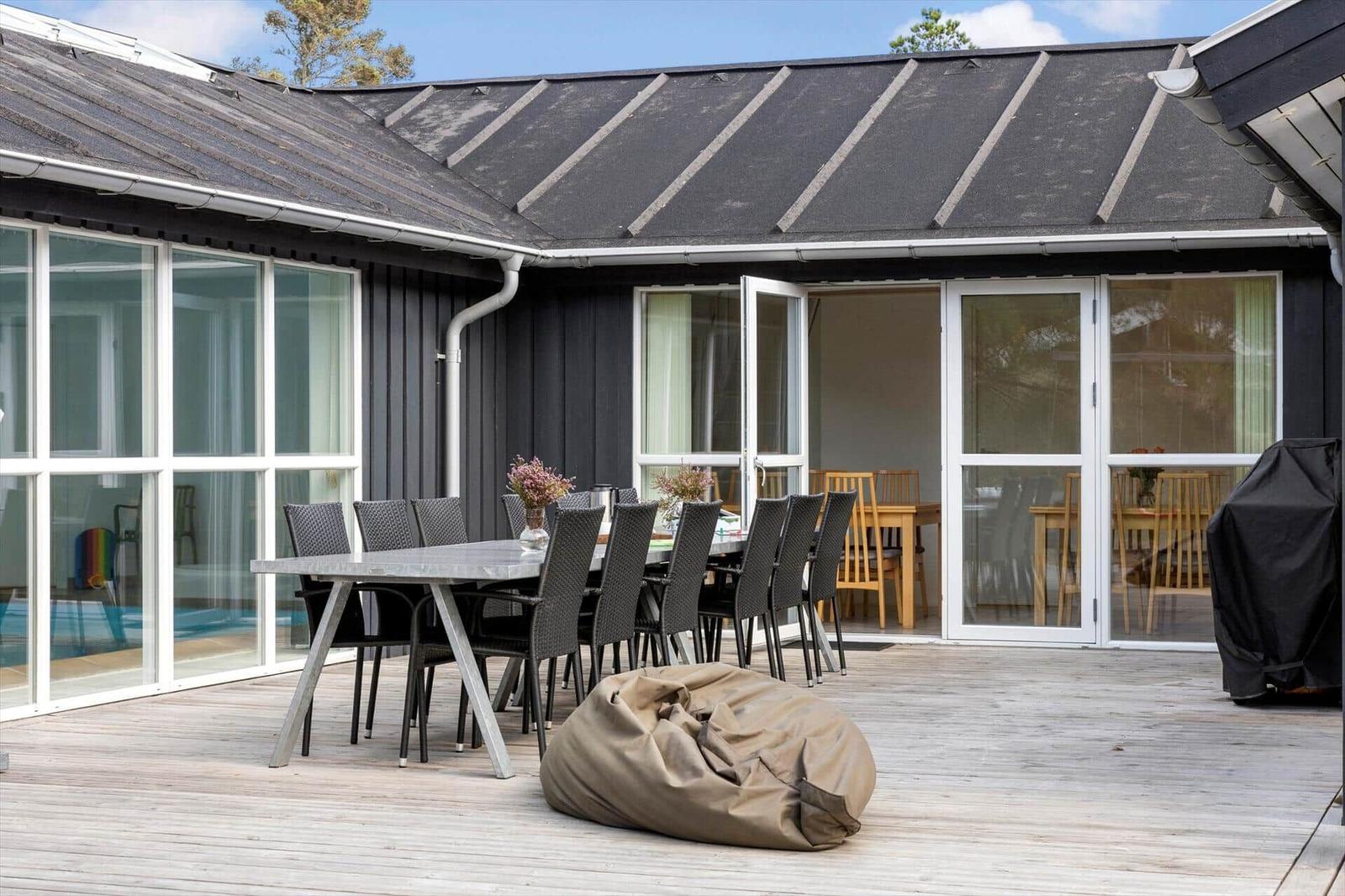 Holzterrasse mit langem Esstisch, Sitzsack und Grill, Innenpool hinter Glas.
